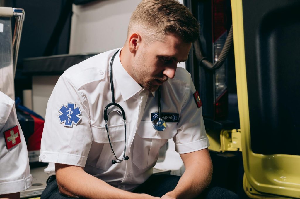 A paramedic in uniform sits pensively inside an ambulance, conveying healthcare dedication.